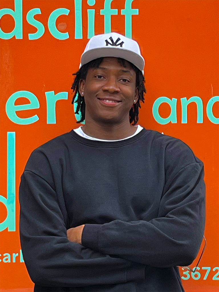 A photo of Patrick smiling as he stands against an orange backdrop